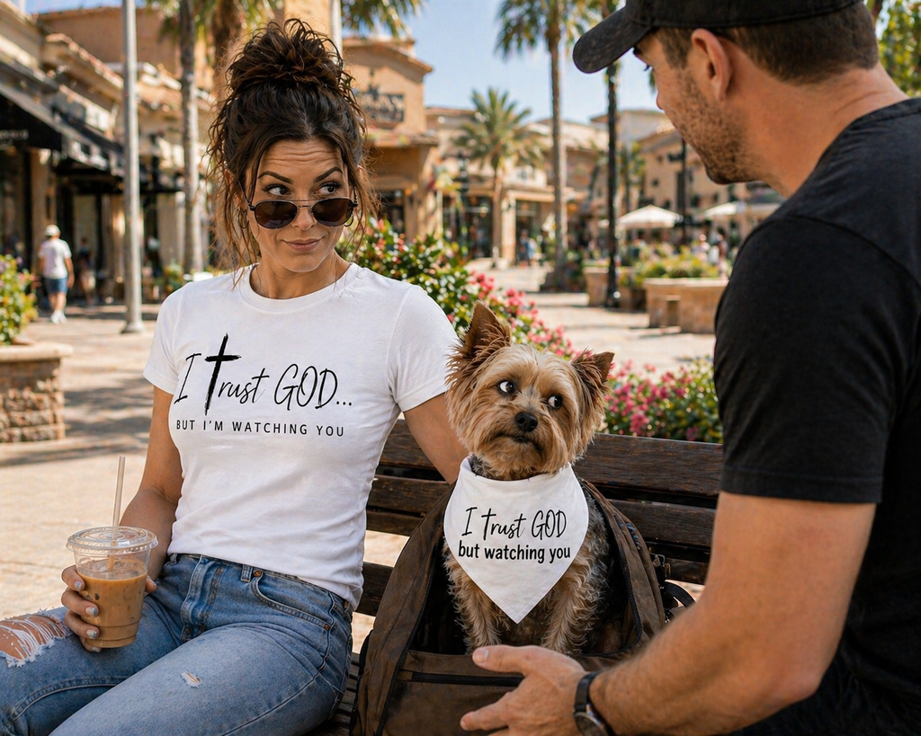 Woman and man sitting on a bench with a dog wearing a matching t-shirt and bandana in a public area.