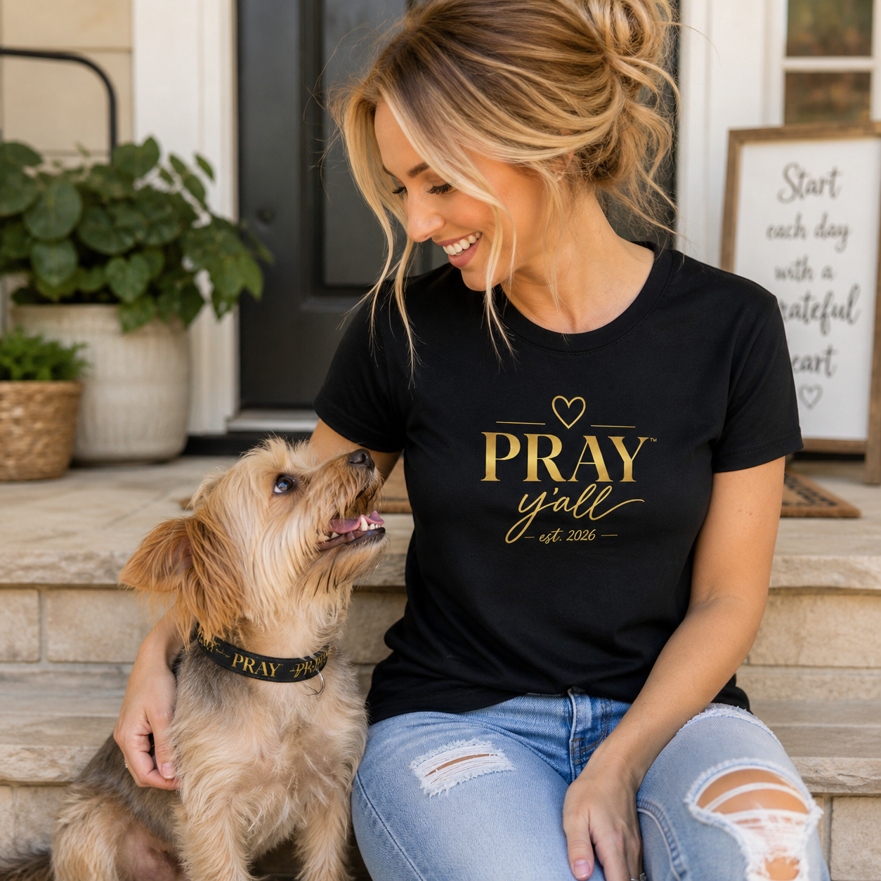 Woman wearing a black t-shirt with 'PRAY yall est 2021' text, sitting on steps with a dog.